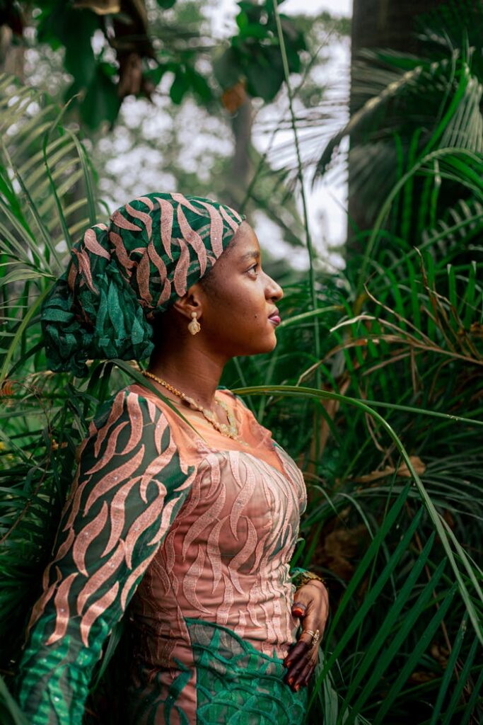 Stylish woman in colorful attire surrounded by lush greenery in an outdoor garden.